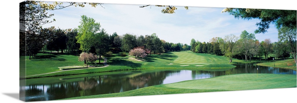 Panoramic photograph of golf course featuring putting green, sand traps, and winding pond.  There are various trees and on...