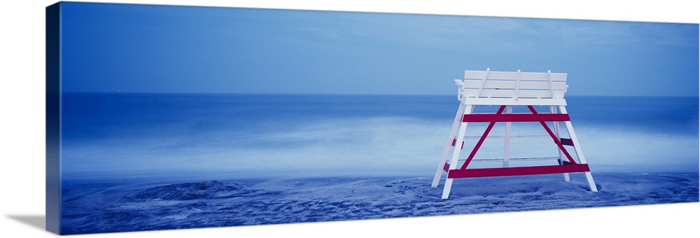 Panoramic photograph on a big canvas of the back of an empty, wooden lifeguard chair sitting on the beach in front of blue...
