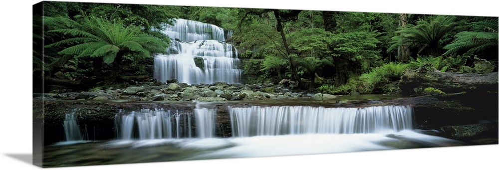 This is a  panoramic landscape photograph of water cascading down a tiered waterfall in a tropical forest.