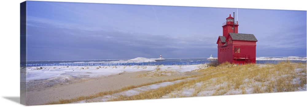 Lonely red light house on the edge of the water on a snowy beach, standing out against the pale cloudy sky.