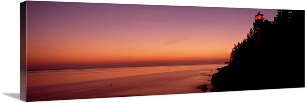 Panoramic photograph taken during a sunset with a lighthouse shown on the right side of the picture atop a hill that is si...