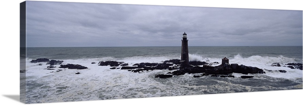 This decorative wall art is a panoramic photograph taken on an overcast day of a lighthouse built on rocks being battered ...