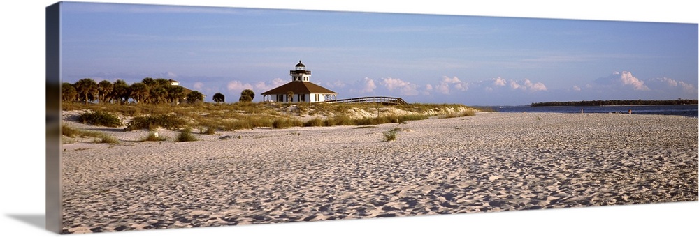 An elongated view of a beach with a lighthouse off in the distance on top of the dunes.