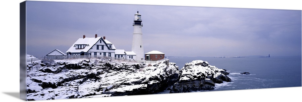 Snow covers the ground and a lighthouse is pictured just at the edge of the rocky cliffs.