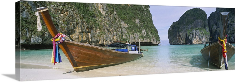 Panoramic photograph of two big canoes docked in sand at the shoreline with huge rock formations in the distance.
