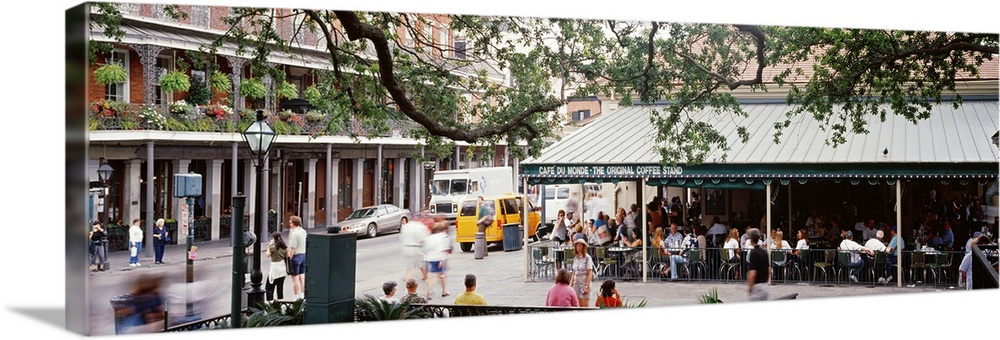 Large panoramic photograph of the French quarter in New Orleans with a tree hovering over and an outdoor restaurant filled...