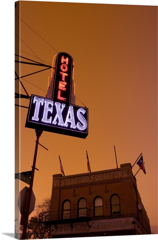 A hotel sign is illuminated under a sunset sky and photographed from below with a view of a furniture store building just ...