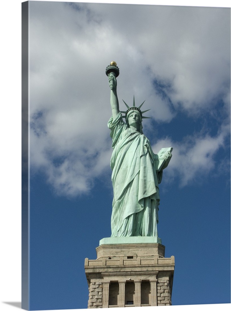 Vertical, low angle photograph on a big canvas, looking up at the Statue of Liberty against a blue sky with thin white clo...