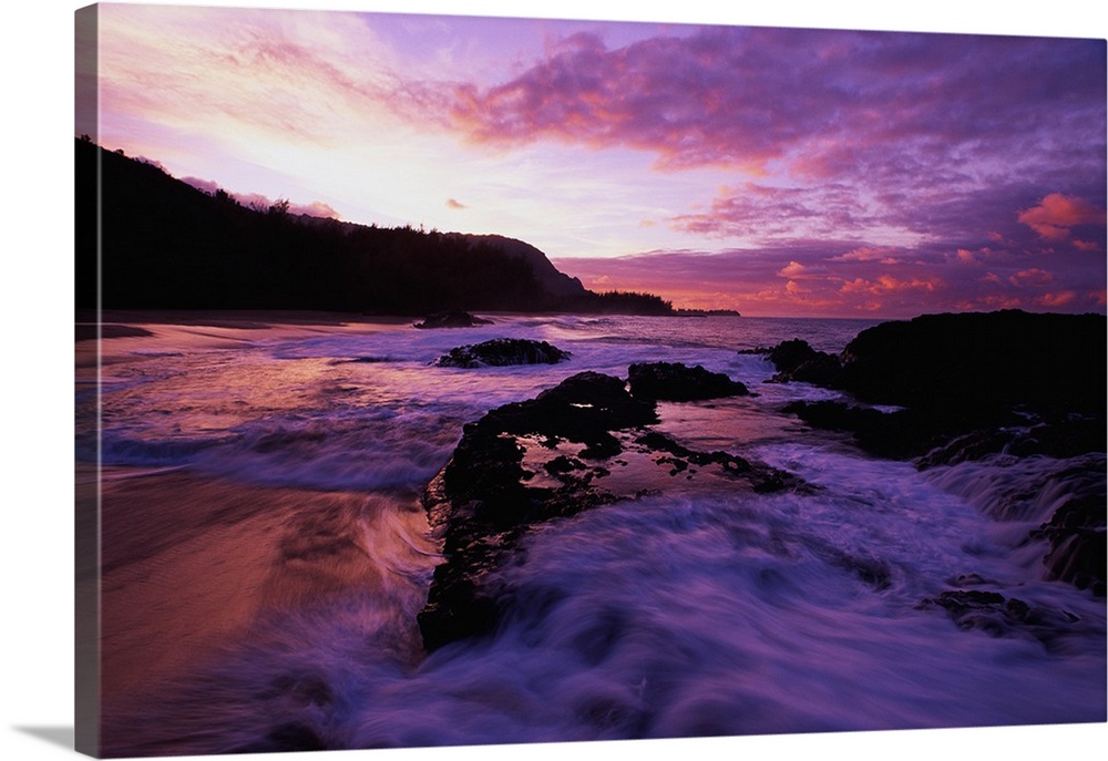 Photograph of rocky shoreline with waves rolling in at dusk.  There is a silhouette of a forest in the background.