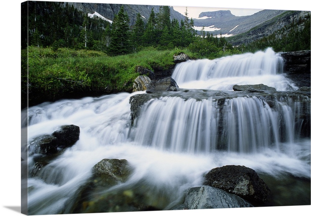 Big print of water rushing down small waterfall areas of rocks in a river surrounded by rugged mountains.