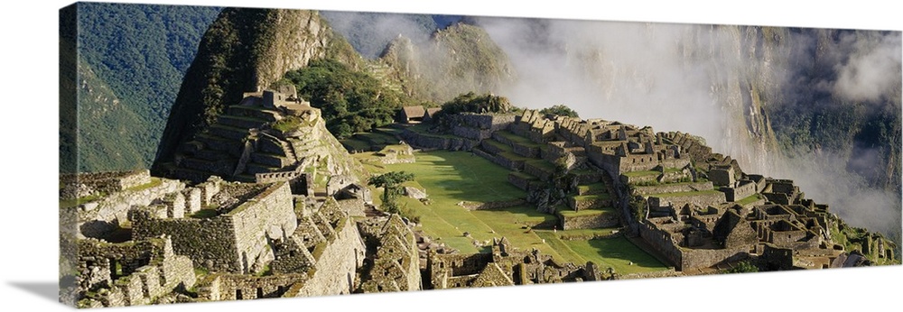 Oversized landscape photograph of Machu Picchu in the sunlight, thin clouds in the background, in Peru.