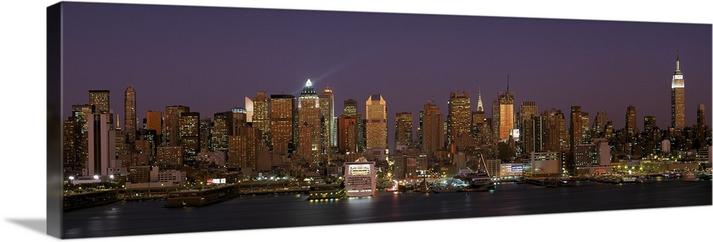 Wide angel, distant photograph of the Manhattan skyline, lit at night, beneath a deep purple sky in New York.