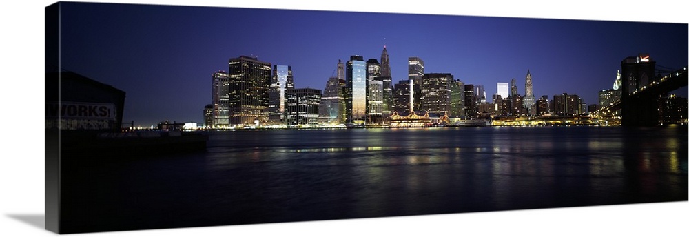 Panoramic photo of the NYC cityscape lit up at night seen from the water.