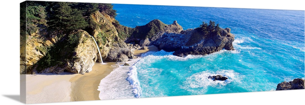 Panoramic photograph of waves from the Pacific ocean crashing into the jagged rocks within McWay Cove in Big Sur, Californ...