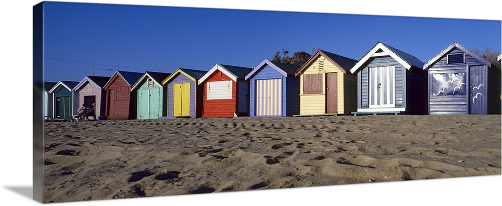 A row of colorful huts are photographed lining the sandy beach.