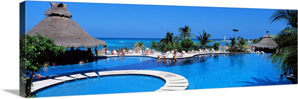 Panoramic photo print of a big pool with people swimming in it with the ocean in the background.