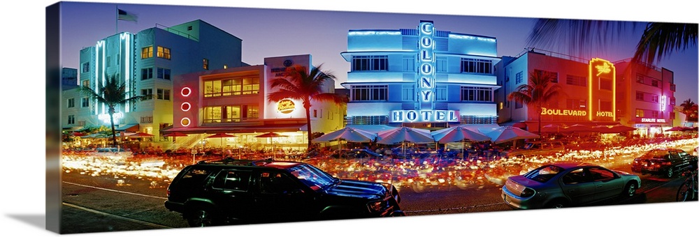 Wide angle, giant photograph of a strip of brightly lit hotels and dance clubs at night, in Miami Beach, Florida.