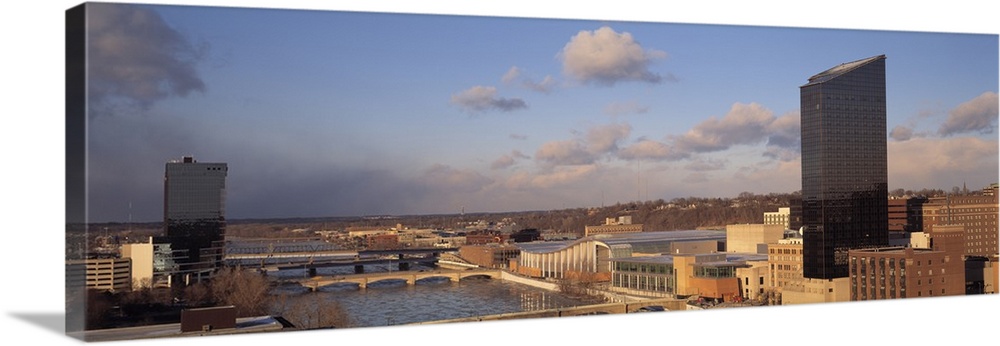 The city skyline in Grand Rapids is photographed in panoramic view with a river cutting in between some of the buildings.