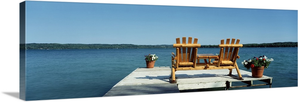 This panoramic photograph is taken from behind two chairs sitting on a dock looking out over a body of water and land in t...