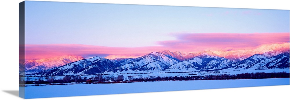 A panoramic snowscape photograph of plains and clouds passing over mountains at the end of the day.