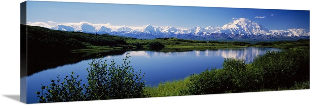 Panoramic photograph of snow covered mountains under a clear sky with rolling grass hills and river in the foreground.