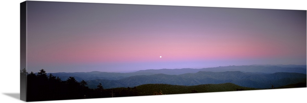 Mountains in the distance are photographed under a sunset sky with a small view of the moon.