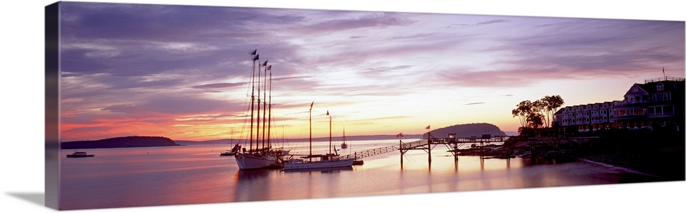 Panoramic photograph sailboats at dock under a cloudy sunset with mountain silhouettes in the distance.