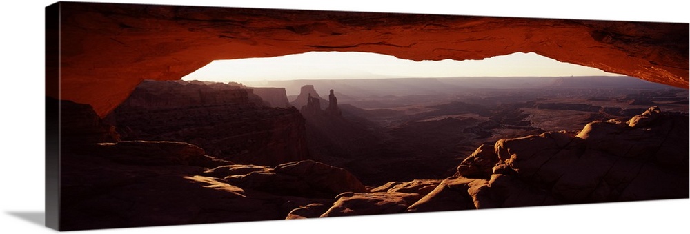 View through a stone arch in the morning, looking over the desert valley of eroded rock.