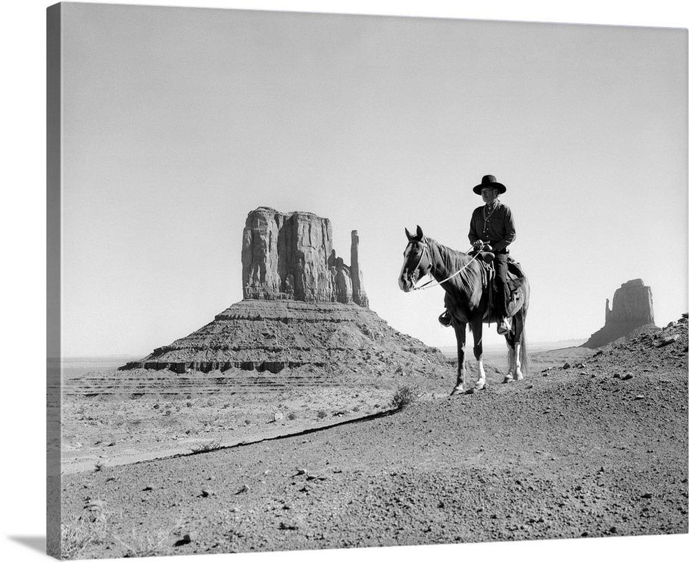 Navajo indian in cowboy hat on horseback with monument valley rock formations in background.