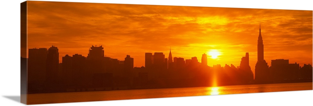 This panoramic photograph shows the sun rising over Manhattan and making silhouettes of the city skyline.