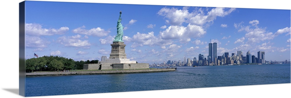 Panoramic picture taken from a distance of the NYC skyline with Ellis Island and the Statue of Liberty to the left.