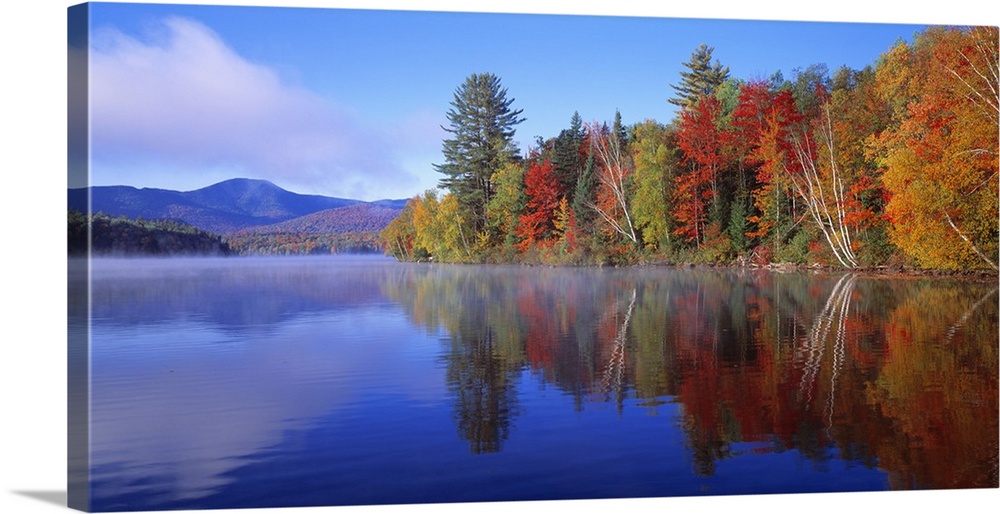 Big, horizontal photograph of autumn trees reflecting along the shoreline of the Franklin Falls Pond in New York, mountain...