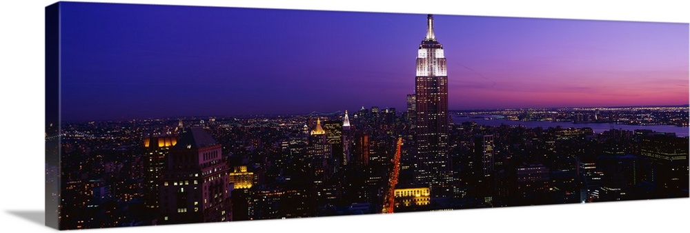 This is a panoramic photograph of the Manhattan skyline at night contrasting with a dramatic and vibrantly hued sky.
