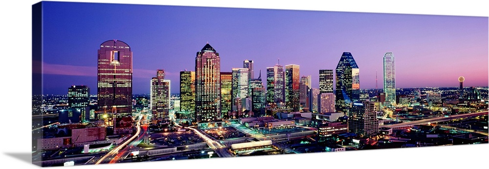Panoramic photograph displays the busy skyline of Dallas, Texas at night.  The bright lights of the skyscrapers and cars c...