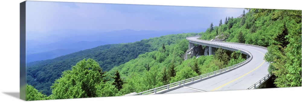 Panoramic photograph of road winding through tree covered mountains.