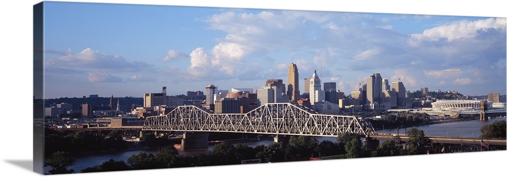 Wide angle photograph taken of the Cincinnati skyline from a distance with a clear view of the bridge into the city.