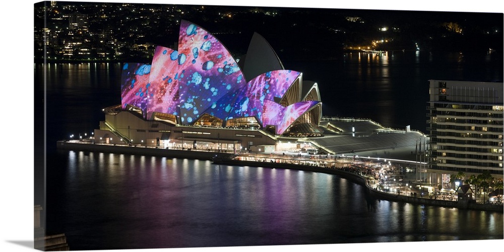 This landscape photograph shows colorful lights and illustrations projected on to this landmark building in a harbor.