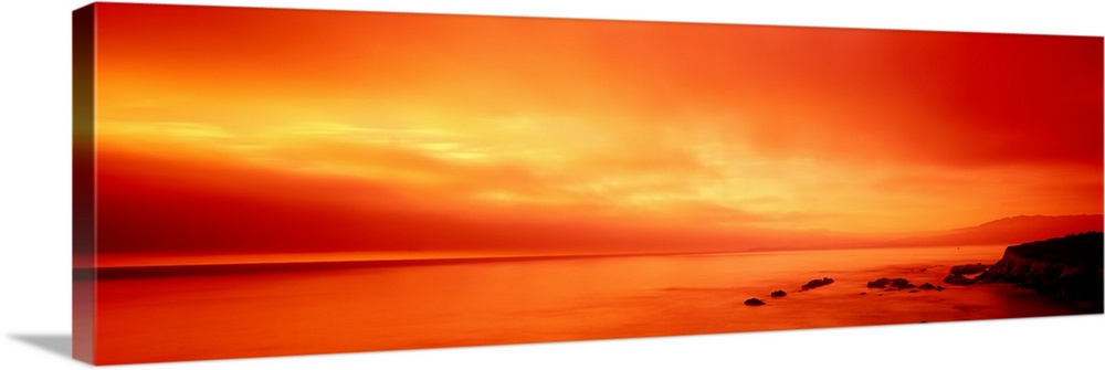 Panoramic photograph displays the vibrant glow of the sun shining over a coastline within the Western United States.  In t...