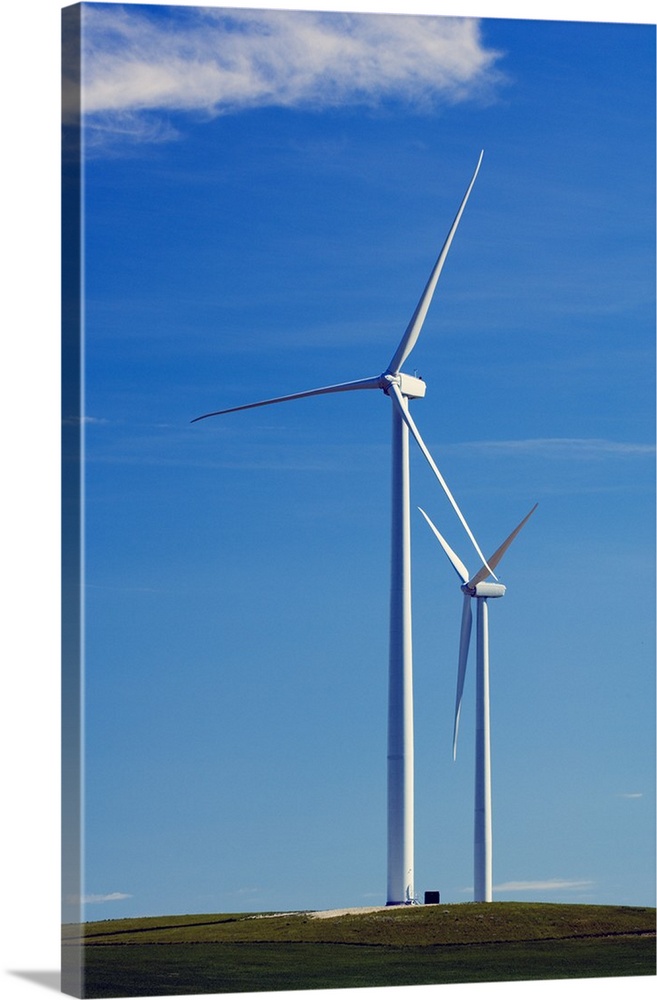 Pair of wind farm turbines in green grass, blue sky, Montana