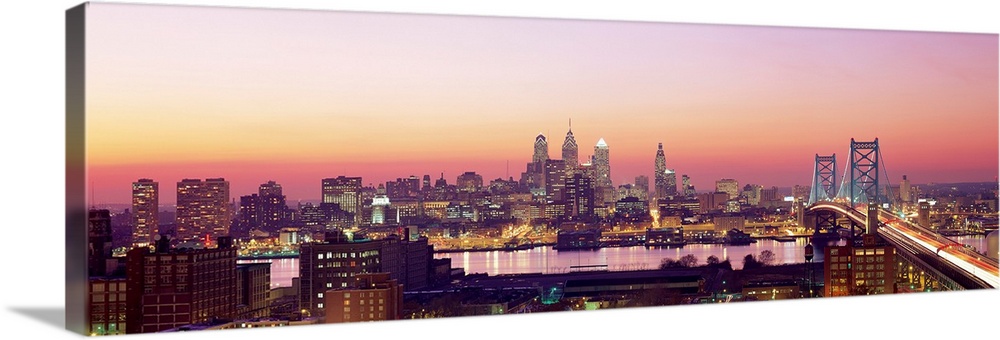 Panoramic photograph displays the busy skyline and Benjamin Franklin bridge in Philadelphia, Pennsylvania at twilight.  Th...