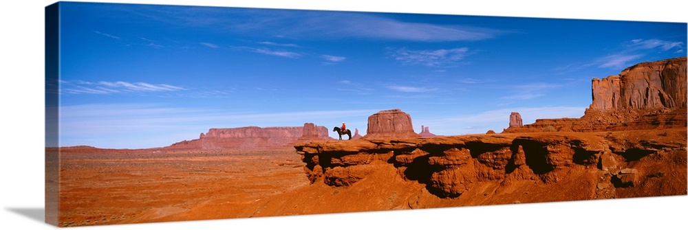 A man on a horse at the edge of a cliff overlooking the arid desert of Monument Valley on a clear day.