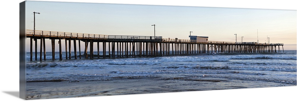 Large landscape photograph of Pismo Beach Pier extending into the waters along Pismo Beach, in San Luis, California, at dusk.