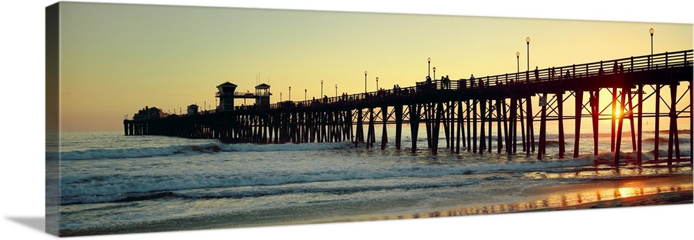 Panoramic wall docor of the silhouette of a pier reaching into the ocean surf at sunset.