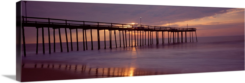 Panoramic photograph of wooden dock stretching into ocean at dusk under a dark cloudy sky.