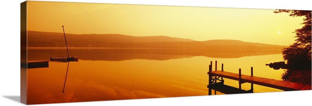 A dock and boat reflect on these still waters at sunrise in this panoramic photograph wall art.