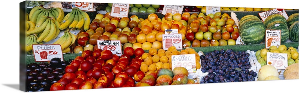 Large, horizontal photograph of a fruit stand with many types of fruit and pricing signage in each section, at the Pike Pl...
