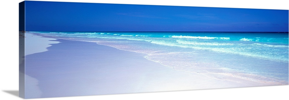 A panoramic wall art picture of a tropical beach with flawless sand and a clear horizon as waves wash up on the shore.