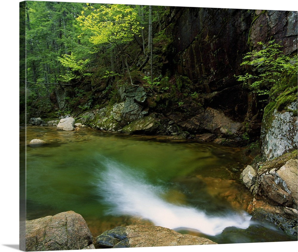 Large horizontal photograph of a pool of water at the bottom of Sabbaday Falls, surrounded by rocks and trees in the White...