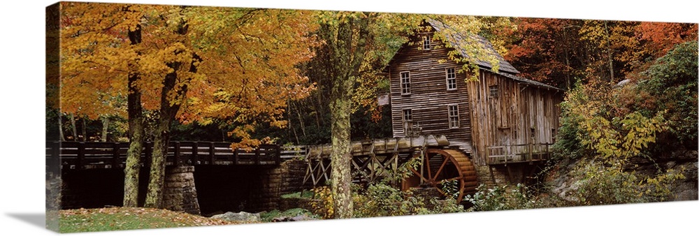 Wide angle view of an old mill surrounded by trees and foliage in the autumn. A small bridge is shown just to the left of ...