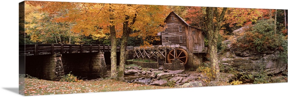 Panoramic photograph of old stone bridge leading to water mill located in a fall forest.
